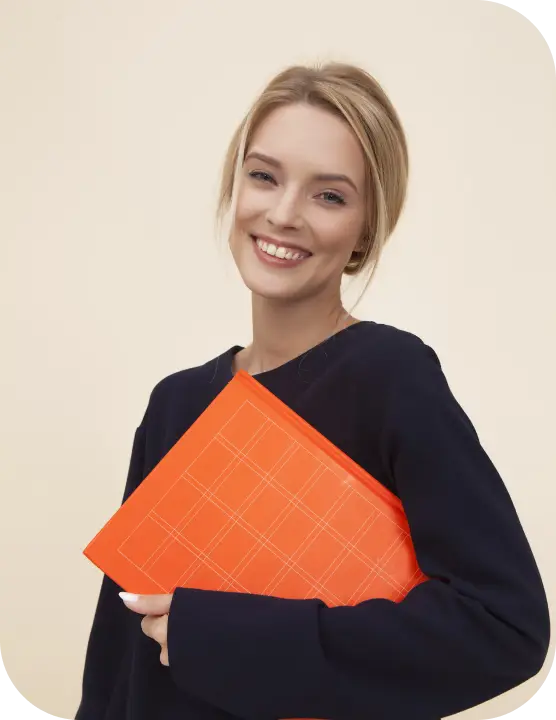 A woman stands confidently, holding an orange folder in her hands, showcasing a professional demeanor.