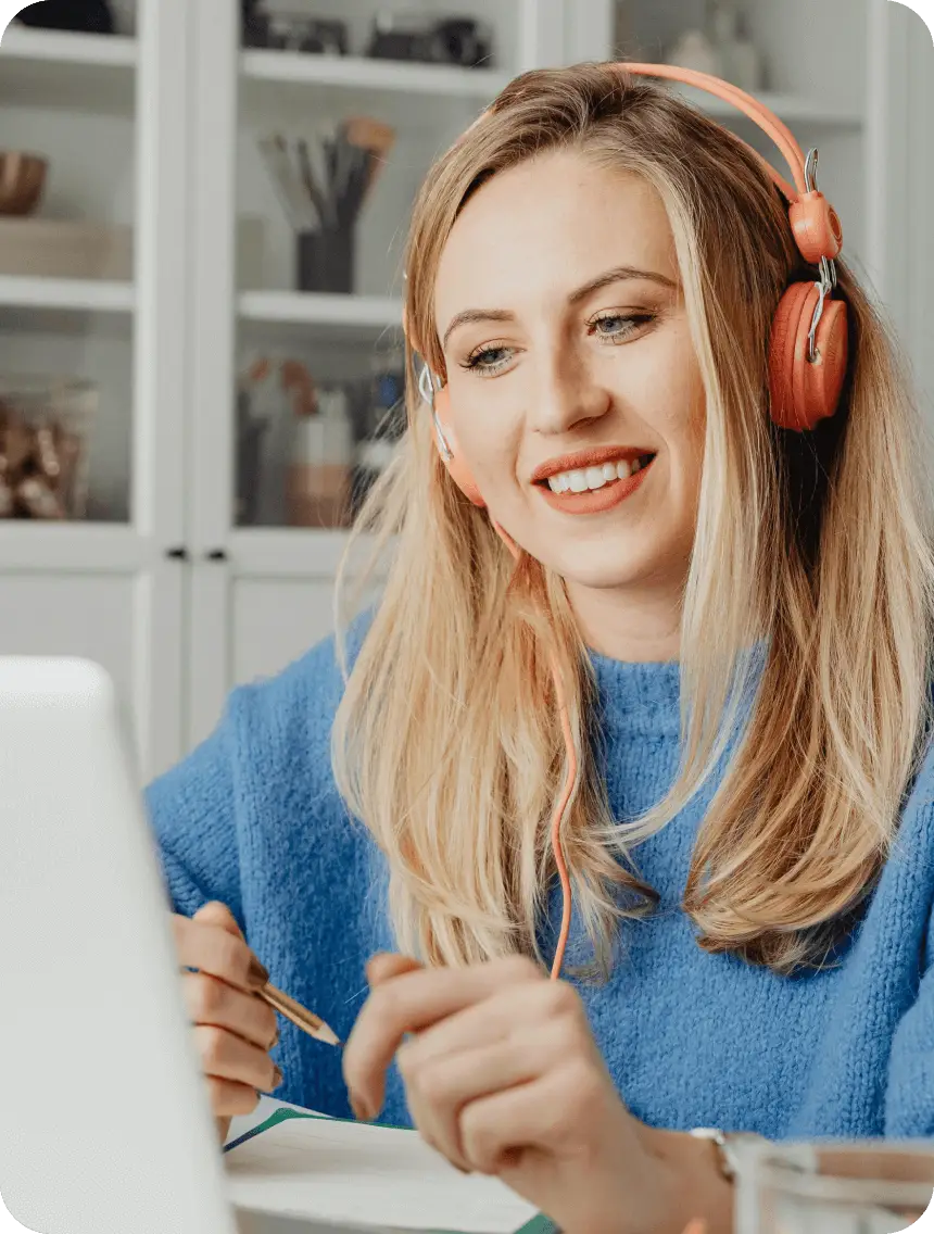 A woman wearing headphones sits in front of a laptop, focused on her work or listening to music.