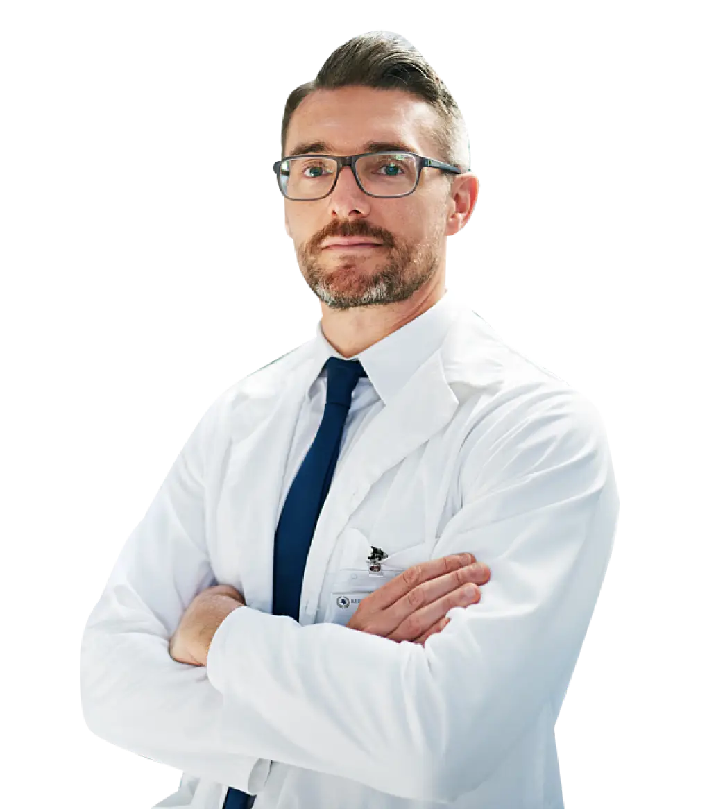 A male provider wearing a lab coat and tie, standing confidently in a clinical setting.